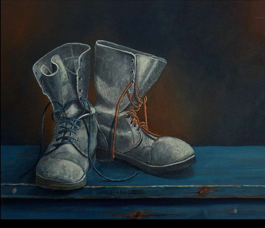 A pair of boots, one with a blue lace and the other with a red lace, resting on a wooden surface.